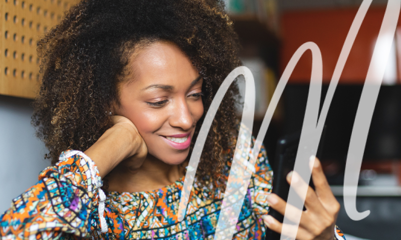 woman with curly hair smiling while looking at her phone