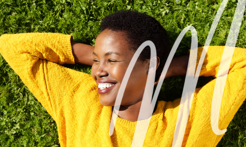 woman in yellow sweater laying on the grass smiling